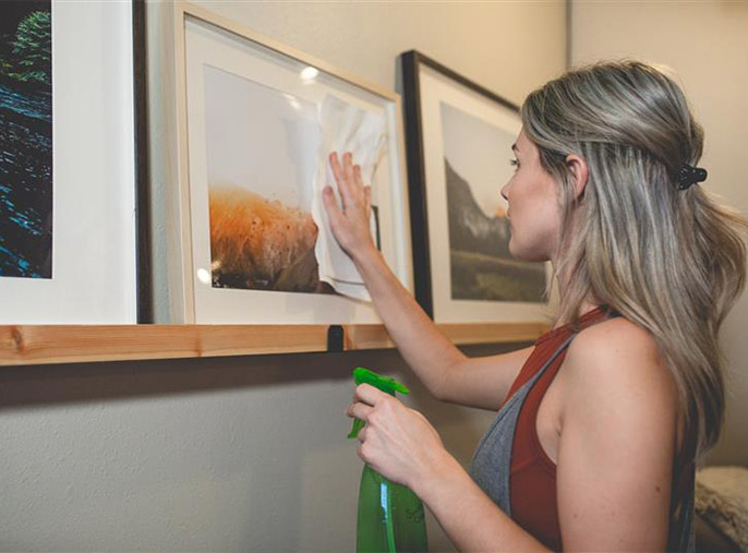 A woman is wiping a picture on the shelf with a paper towel