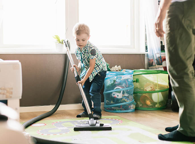 A little boy helping clean by vaccuming an area rug